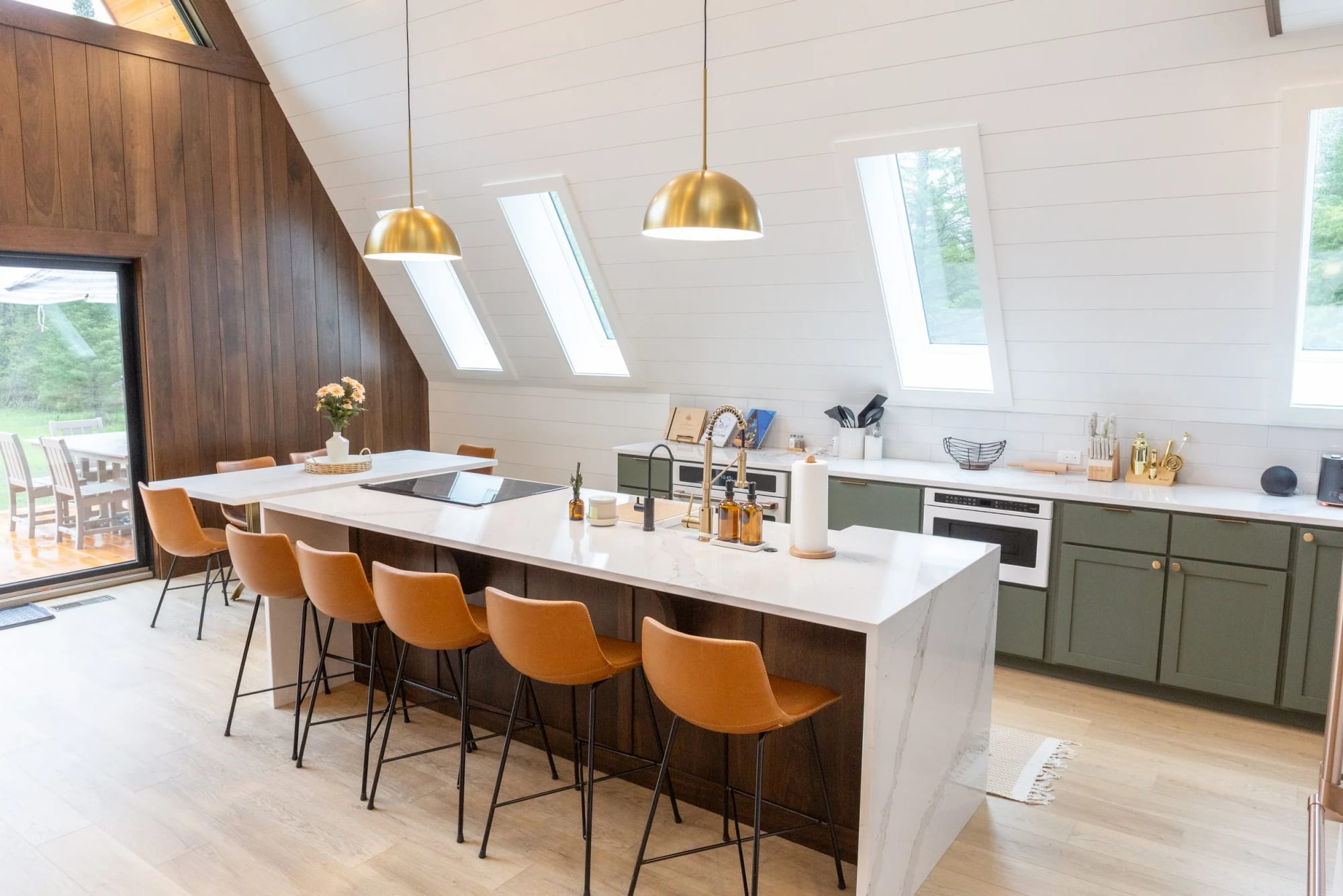 Bar stools along the kitchen island under brass pendants